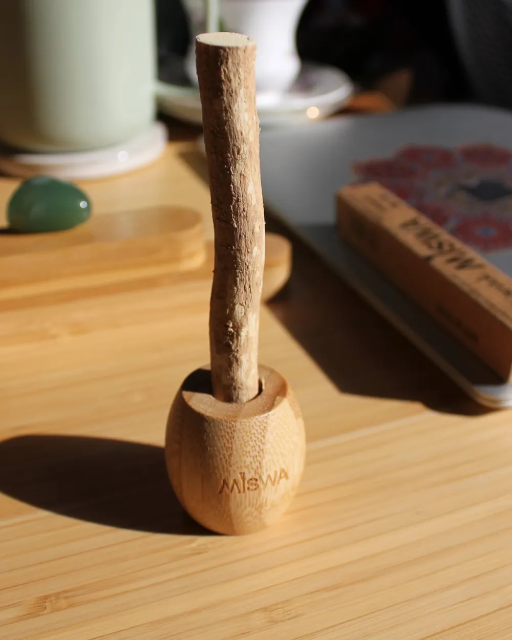 Un siwak MISWA debout dans son porte-siwak en bambou, sur une table en bois, avec son étui kraft à l'arrière-plan